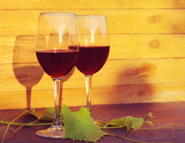 İki kadeh kırmızı şarap ve üzüm yaprakları bir ahşap yüzeye