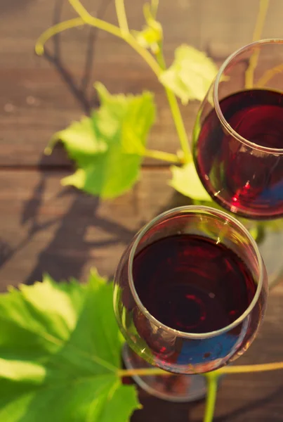 Két pohár vörös bor és a szőlő levelek, a fa felületén — Stock Fotó