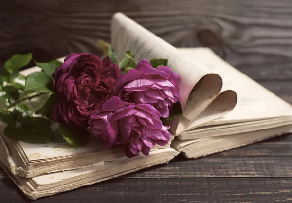 Rosarote Rosen und das alte Buch auf einem Holztisch im Vintage-Stil. — Stockfoto