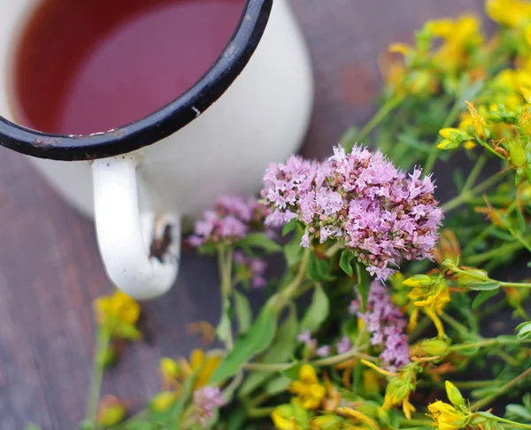 Tee im eisernen Becher und Heilkräuter auf einer Holzoberfläche. — Stockfoto