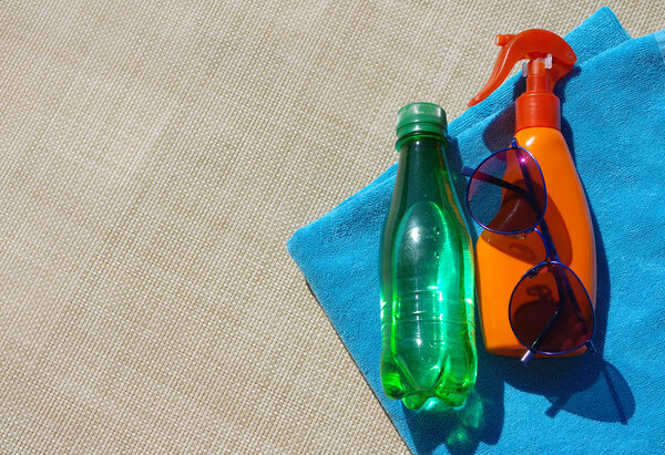 Sunblock cream, sunglasses and small bottle with water and a blue beach towel.
