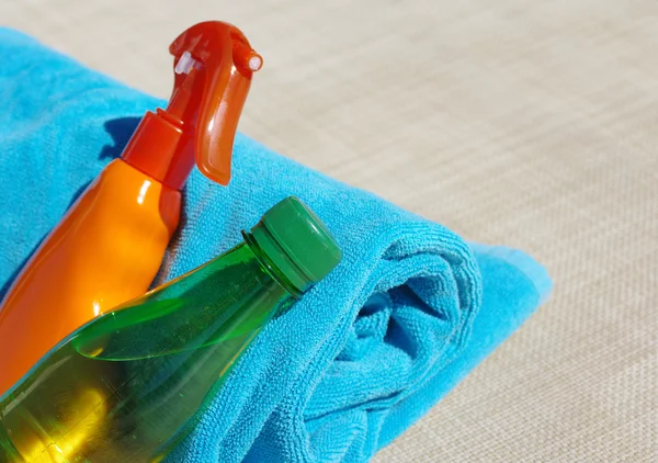 Sunblock cream, small bottle with water and a blue beach towel.