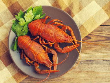 Bir bez ahşap arka plan üzerinde yuvarlak bir kahverengi tabağa haşlanmış crawfishes