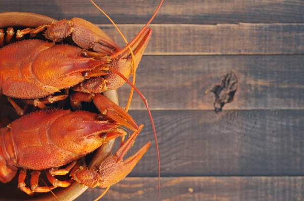 Écrevisses bouillies dans une assiette ronde en bois sur un fond en bois — Photo