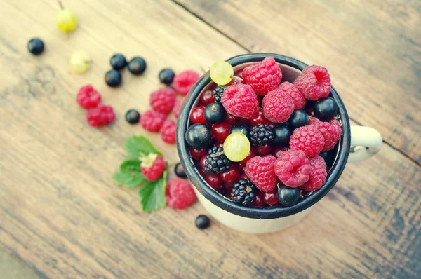Свежие сочные ягоды, малина, смородина, ежевика, крыжовник в старом белом железном кружке — стоковое фото