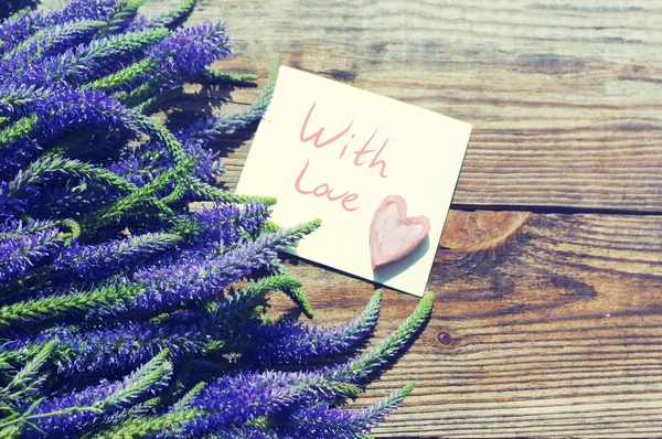 Bouquet di fiori blu selvatici estivi, un cuore decorativo e la carta bianca con l'iscrizione "Con amore" sul vecchio sfondo di legno — Foto Stock