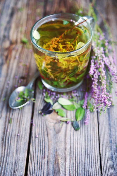 Herbal tea in a transparent glass mug and forest herbs on a wooden surface of a table.