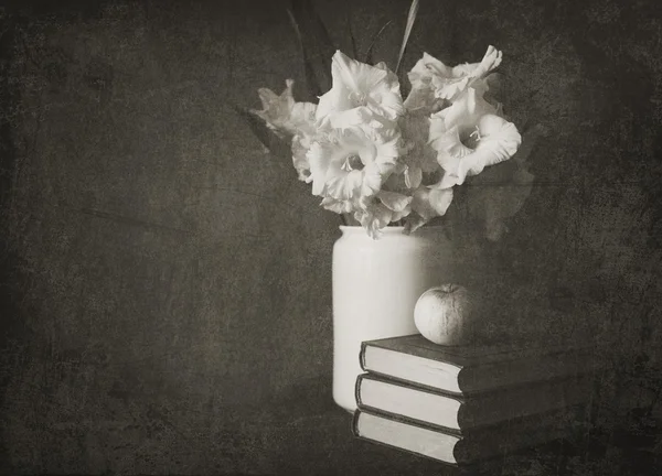 Gladiolos en una jarra blanca con libros y manzana, la foto vieja hecha en blanco y negro — Foto de Stock