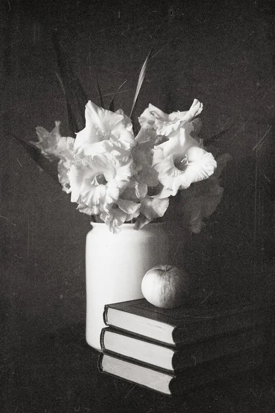 Gladioli in una brocca bianca con libri e mela, la vecchia foto in bianco e nero — Foto Stock