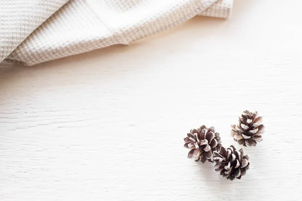 クリスマスの背景 白いキッチンタオルや布ナプキンと白い木製のテーブルの上に3つの松のコーン コピースペース付きのトップビュー — ストック写真