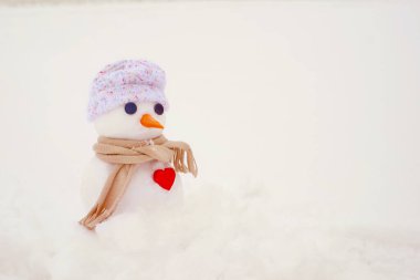 Şapkalı şirin bir kardan adam ve karda kırmızı kalpli bir eşarp, yakın plan. Bir kardan adamla tatil kartı.