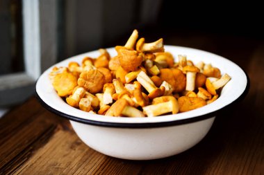 Tahta bir yüzey üzerinde demir bir kasede taze chanterelle mantarları yakın plan, yumuşak seçici odaklanma