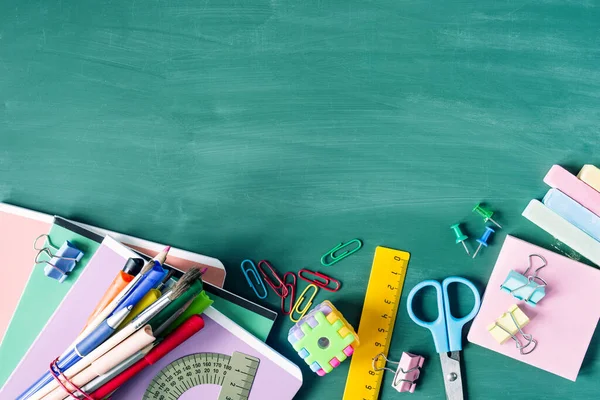 Back to school background. School supplies, pens, pencils, notebooks, ruler, scissors on a  against the background of a green school board, copy space, top view.