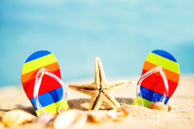 Plaj yaz tatili. Mavi denizin arka planında parlak parmak arası terliklerle ve deniz yıldızıyla seyahat edin, yakın plan, yumuşak odak. 