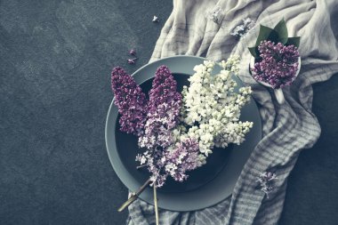 Yuvarlak gri tabaklar üzerinde beyaz ve pembe leylaklar ve koyu bir yüzey üzerinde çizgili pamuklu şal, tonlu, üst manzara, boşluk kopyala.