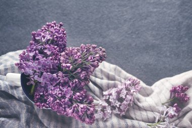 Bir kaptaki pembe leylak demeti çizgili pamuklu atkı üzerinde koyu renk bir yüzey, tonlu, üst görünüm, boşluk kopyala.