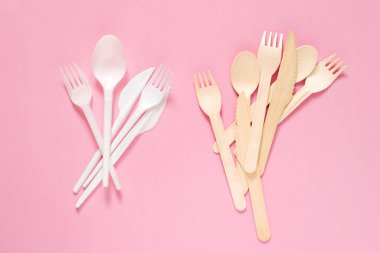 Plastik ve ahşap çatallar, kaşıklar ve bıçaklar pembe bir yüzeye yakın çekim, üst manzara. Plastik yok, ekolojik sofra takımı yok, ayrıştırılabilir sofra takımı yok. Çevre koruması