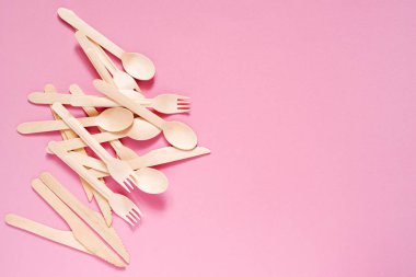 Tahta çatallar, kaşıklar ve bıçaklar pembe bir yüzeyde, üst manzara, kopyalama alanı. Eko sofra takımı, biyolojik olarak bozunabilir sofra takımı. Çevre koruması