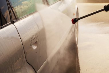 Adam arabasını yıkama makinesinde su basıncıyla yıkıyor.