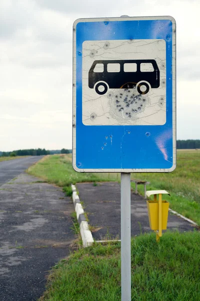 Old road blue bus stop sign damaged by pistole bullets by asphalt road