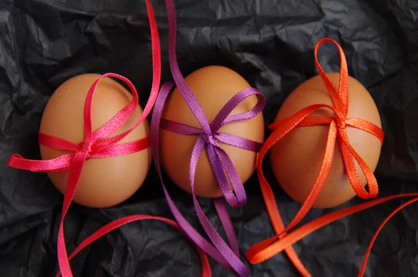 Três ovos de Páscoa com fitas coloridas brilhantes em papel enrugado preto — Fotografia de Stock