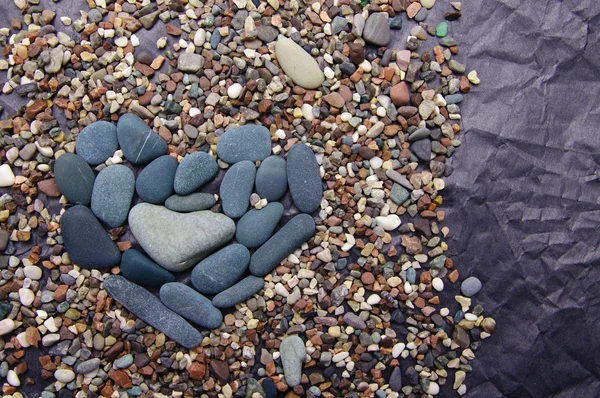 Pedras de cor do mar na forma de coração contra papel preto amassado — Fotografia de Stock