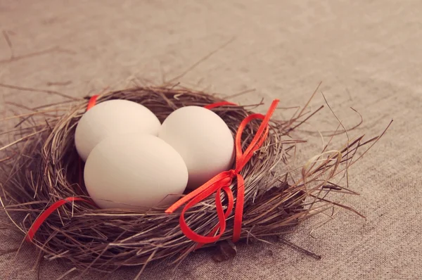 Three Easter white eggs in a nest from a dry grass — Stock Photo, Image