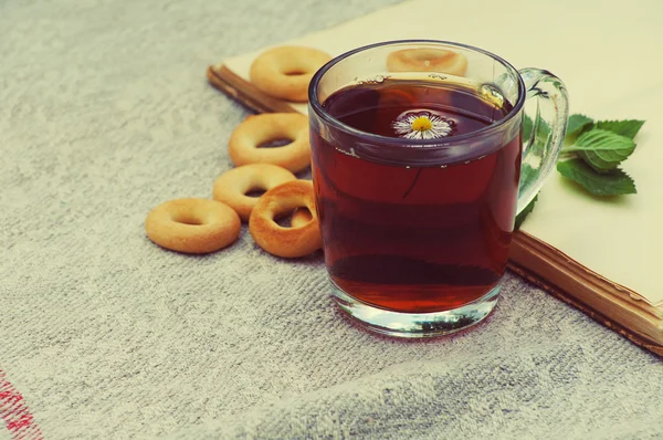 Tea in a glass mug, bagels and the open book with a mint leaflet on a linen cloth — Stok fotoğraf