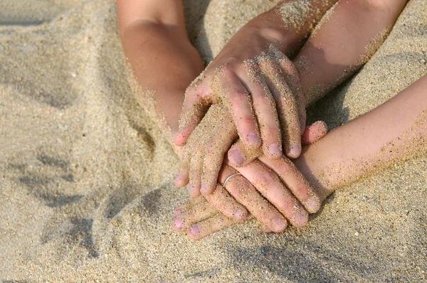 Moeder en zoon met elkaar verweven handen op een strand. — Stockfoto