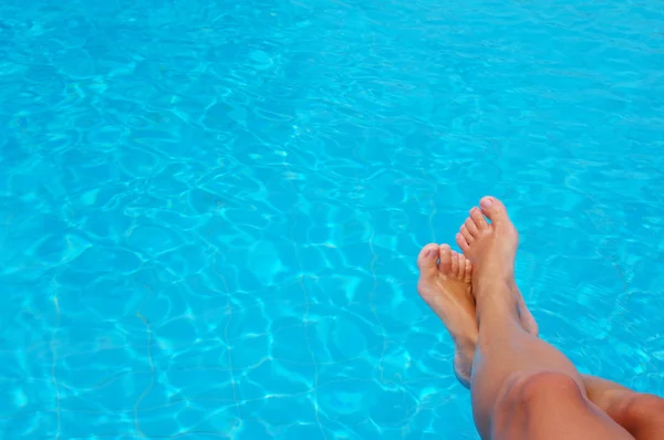 Woman's feet against blue water of the pool.