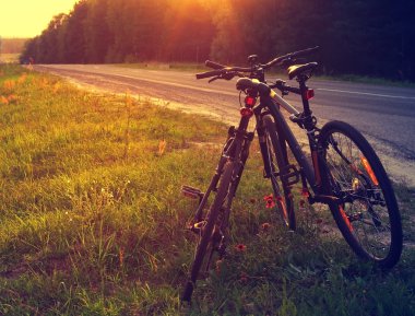 Two road bicycles nearby with each other near the road. Romantic couple of bicycles against the leaving sun
