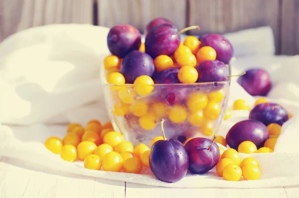 Fresh juicy plums and yellow cherry plum in a glass transparent bowl.