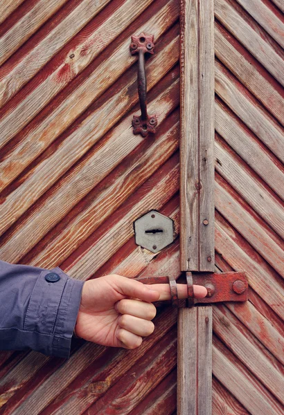 Ancient wooden door and male hand with a forefinger in a key aperture. — Stockfoto