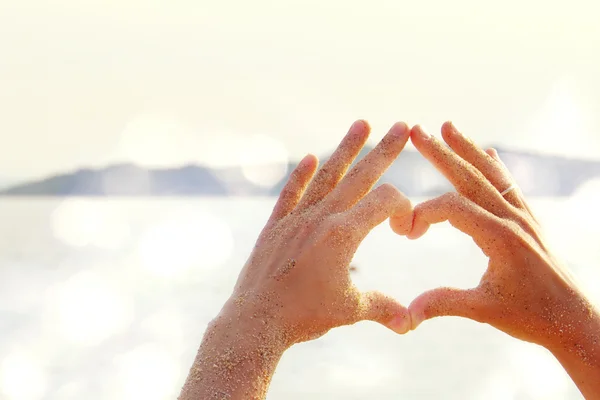 Vrouwelijke handen in de vorm van hart tegen de zee. Handen in de vorm van liefde hart — Stockfoto