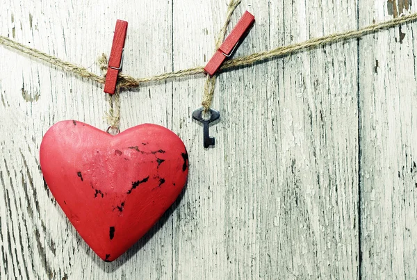 Coração vermelho e pequena chave de metal em pinos de pano de madeira no varal no velho fundo de madeira gasto. Imagem romântica festiva do Dia dos Namorados — Fotografia de Stock