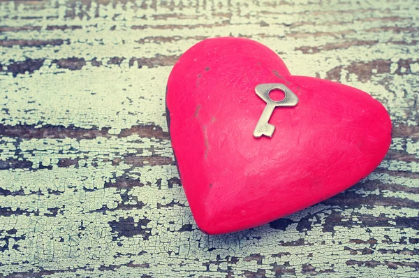 Coração vermelho e pequena chave de metal em um fundo velho de madeira . — Fotografia de Stock