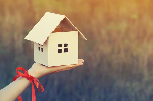 Будинок з паперу на жіночій руці з червоною стрічкою. Концепція зображення продажу або придбання будинку, подарунок . — стокове фото