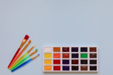 Çocukların yaratıcılığı, hobileri, çizim konsepti. Bir palet suluboya boya ve mavi arka planda beş renkli küstah, yukarıdan bir manzara.