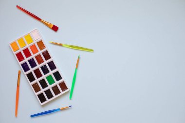 Çocukların yaratıcılığı, hobileri, çizim konsepti. Bir palet suluboya boya ve mavi arka planda beş renkli küstah, yukarıdan bir manzara