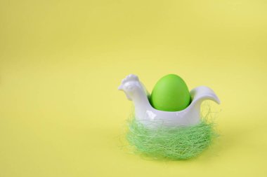 Sarı arka planda tavuk şeklinde bir standa boyanmış yeşil yumurta. Paskalya Bayramı için dekorasyon.