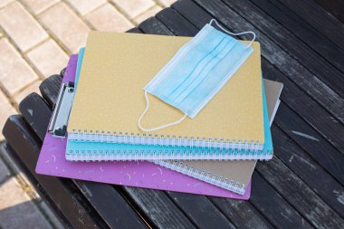 Renkli okul defterleri ve koruyucu bir maske sokakta bir bankta yatıyor. Salgından sonra okula geri dönüyorum. Eğitim kavramı, sağlık koruması, tıp