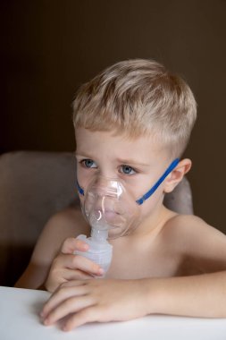 Üzgün küçük bir çocuk evde nebulizörle nefes alıyor, hasta. Evde öksürük ve astım için yardım. Sağlık kavramı.