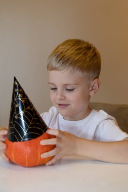 Mutlu gülümseyen çocuk Cadılar Bayramı için elinde kağıt şapkayla balkabağı tutuyor. Çocukluk, Cadılar Bayramı, dekorasyon konsepti. Cadılar Bayramı için fikir.