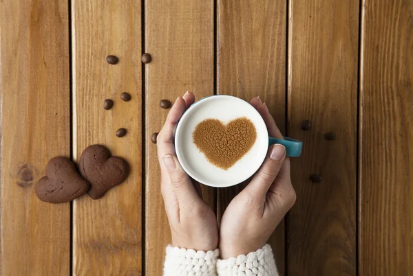 Female hands holding cup of coffee and cookies on wooden table. — Stock Photo, Image