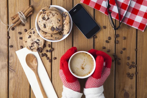 Hands in gloves holding hot cup of coffee and chocolate cookie — Stock Photo, Image