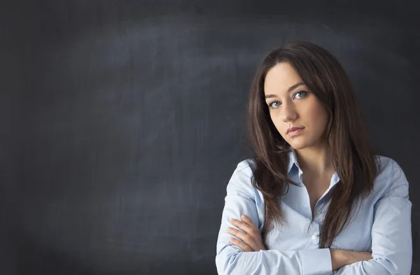 Serious businesswoman standing with arms crossed at blackboard — Stock Photo, Image