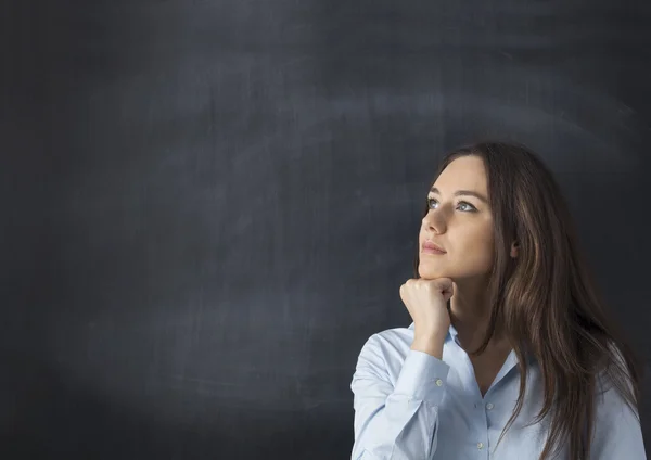 Doordachte jonge vrouw op schoolbord achtergrond — Stockfoto