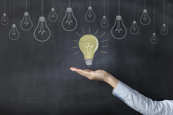 Hand holding light bulb on blackboard — Stock Photo, Image