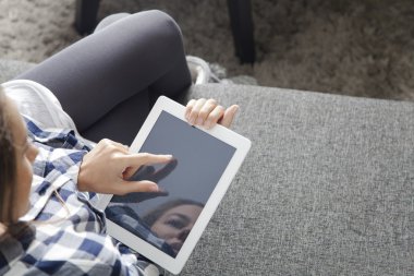 Oturma odasında kanepede oturan ve dijital tablet kullanarak genç kadın