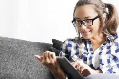 Oturma odasında kanepede oturan ve tablet kullanan genç bir kadın..